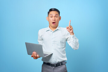 Excited young handsome businessman having a creative idea while holding a laptop on blue background