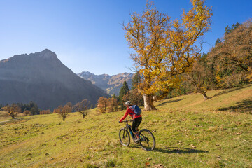 pretty woman riding her electric mountain bike in the mountains of Hinterstein Valley in the upper Allgaeu on warm autumn day, Bavaria, Germany