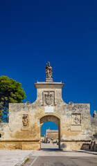 Fototapeta na wymiar The small fortified village of Acaya, Lecce, Salento, Puglia, Italy. The large stone-paved square. The gateway to the city, with the large arch and the stone statue.