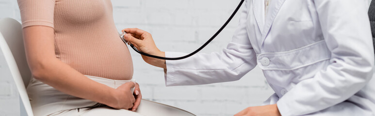 partial view of doctor examining belly of pregnant woman with stethoscope, banner