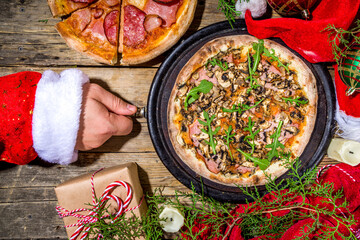 Christmas decorated background with pepperoni and mushrooms pizza,with Santa hands take pizza slice. Delivery, restaurant Xmas Lunch party menu, Santa delivers pizza for Christmas, wooden table above