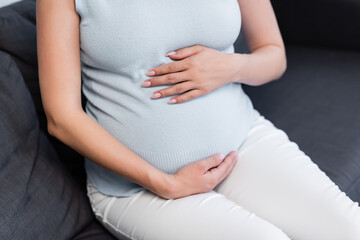partial view of pregnant woman hugging belly while sitting on couch