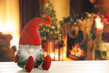 Fototapeta premium Funny Christmas gnome on white wooden table in room with festive decorations. Space for text