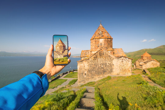 tourist hand taking pictures on his smartphone using photo app. At the background - Lake Sevan and the famous Armenian monastery Sevanavank