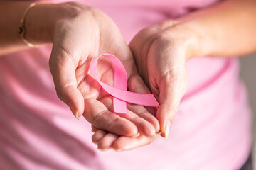 Detail of woman holding pink ribbon in her folded palms, the symbol of breast cancer prevention need