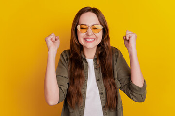 Photo of young cheerful girl ask beg hold fists in victory isolated on yellow background