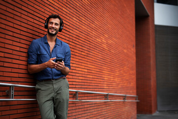 Young man listening to music. Urban fashion man with headphones enjoying the city.