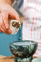 A male chef grinds spices and herbs in a cooking mortar