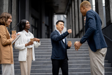 Multiracial businessteam bumping fists each other on city street. Concept of modern successful business people. Idea of business cooperation. Remote and freelance work. Joyful people wear formal wear
