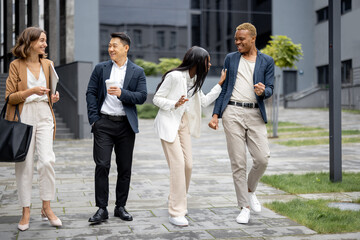 Multiracial businessteam walking and talking on city street. Concept of modern successful business people. Idea of business cooperation. Remote and freelance work. Joyful people wearing formal wear