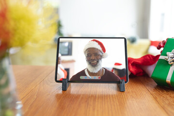 Smiling senior african american man in santa hat on tablet christmas video call interface screen