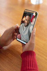 Hands holding smartphone with smiling african american man on christmas video call interface screen