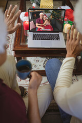 Two men waving to smiling caucasian couple in santa hats on laptop christmas video call screen