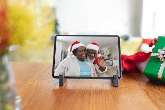 Smiling senior african american couple in santa hats waving on tablet christmas video call screen