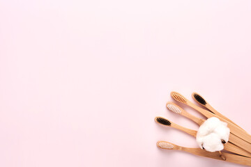 Teeth hygiene and oral dental care products on pink color background with copy space. Eco-friendly bamboo toothbrushes and cotton flowers. Flat lay, top view composition, mockup. Morning concept.