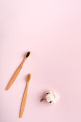 Teeth hygiene and oral dental care products on pink color background with copy space. Eco-friendly bamboo toothbrushes and cotton flowers. Flat lay, top view composition, mockup. Morning concept.