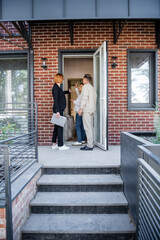 redhead realtor in glasses pointing with finger at house while talking with interracial couple