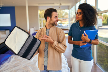 An African American female salesperson consultant advises a man who is holding a mattress sample in a bed, mattress and pillow store.
