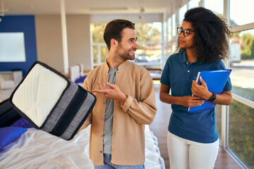 An African American female salesperson consultant advises a man who is holding a mattress sample in...