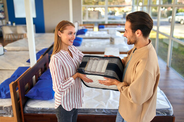 A young couple holds a cutaway mattress sample in a bed, mattress and pillow store. Everything for...