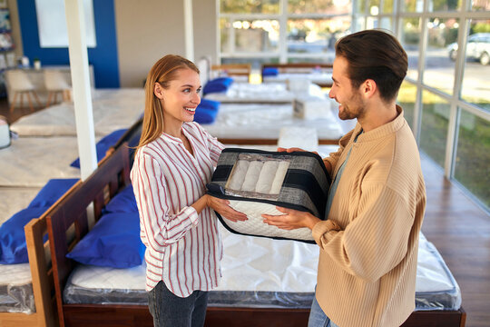 A Young Couple Holds A Cutaway Mattress Sample In A Bed, Mattress And Pillow Store. Everything For A Comfortable Sleep.