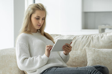 Happy pregnant woman uses a digital tablet while sitting on the sofa in the living room