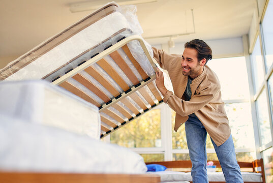 A man chooses a bed in a store, examines a frame with slats. Purchase of a mattress, bed and other sleeping accessories.