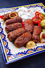 Traditionelle kroatische Cevapi als würzige Fleischbällchen mit Barbecue Gemüse und Zaziki serviert als Draufsicht auf einem rustikalen Teller  - obrazy, fototapety, plakaty