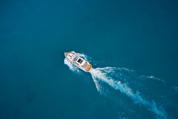 Top view of a white high-speed boat. Yacht movement on blue water top view. Luxury yacht on the water aerial view. White yacht fast movement on the water top view. Travel - image.
