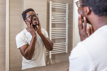 Attractive Well-Shaved African American Man Touching Smooth Face After Shaving Caring For Skin Standing Shirtless Near Mirror In Modern Bathroom Indoor. Male Facial Skincare Routine. Selective focus