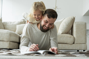 Bearded father reads a fairy tale for his little daughter lying on the floor of the house. Happy...