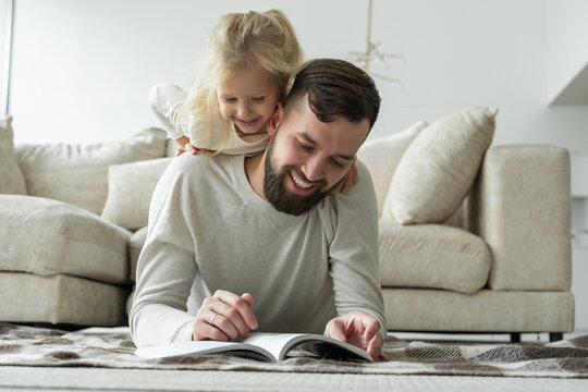 Bearded father reads a fairy tale for his little daughter lying on the floor of the house. Happy family lying on the living room floor