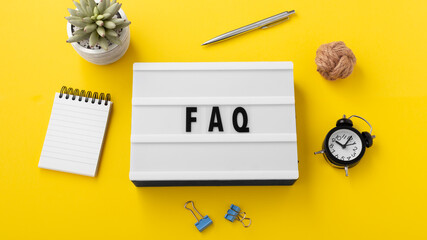 FAQ word on lightbox with office supplies on yellow background