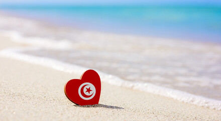 Flag of Tunisia in the shape of a heart on a sandy beach. The concept of the best vacation in...