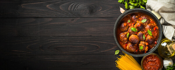 Meatballs in tomato sauce and pasta spaghetti on dark wooden table. Food cooking background. Long banner format.