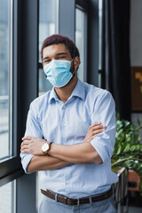 African american businessman in medical mask standing with crossed arms in office