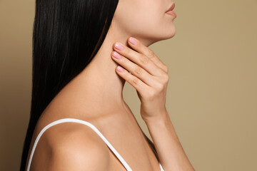 Young woman doing thyroid self examination on beige background, closeup