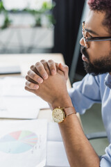 Side view of african american businessman in eyeglasses sitting near blurred papers in office