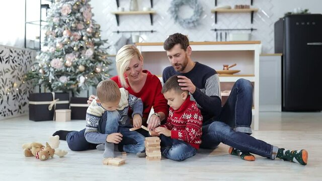 Affectionate parents and cute children playing with wooden cubes in a cozy home, enjoying a smart game, relaxing on a warm floor in the living room together near a christmas tree