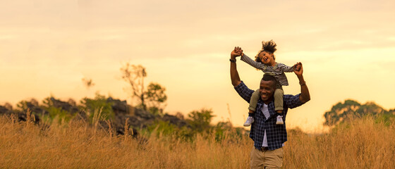 Happy African family child daughter riding the neck father and running on meadow nature on...