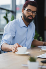 Cup of coffee on table near blurred african american businessman in office