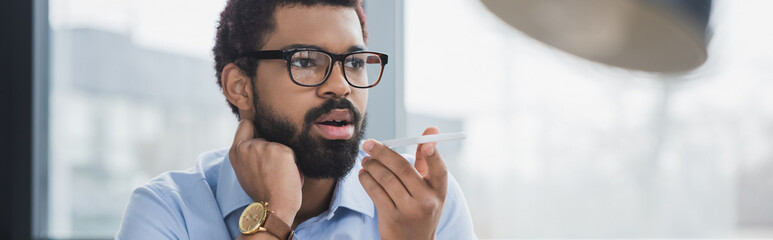 African american businessman in eyeglasses recording voice message on smartphone, banner