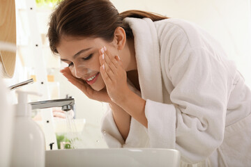 Beautiful teenage girl washing face with cleansing foam in bathroom. Skin care cosmetic