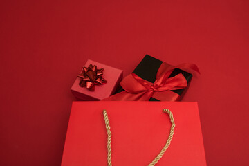 Creative look, two red and black gift boxes and a red shopping bag on a red background. Black Friday, discounts, sales, Christmas shopping on a red background, a place for text, a black gift box with