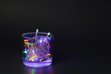Glass with Christmas lights on black background.