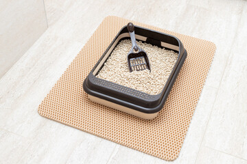 Cat toilet tray with wooden pellets and scoop on litter mat in bathroom. Pet hygiene. top view