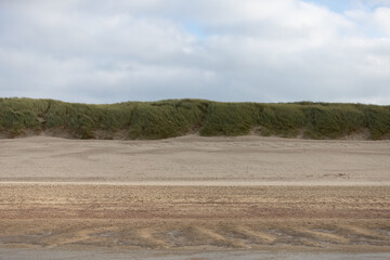 Fototapeta na wymiar Sand at the beach, dune with grass in the background, cloudy sky
