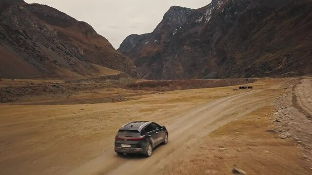 A black SUV jeep car is driving along an empty country road in the huge Katu-Yaryk canyon Chulyshman Valley with a large mountain bubbling river. Altai, Siberia, Russia. People travel along a dirt