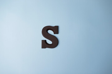 Letter of the alphabet S is made from dark milk chocolate on blue background.