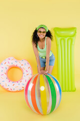 full length of positive african american woman near inflatable ball, mattress and ring on yellow